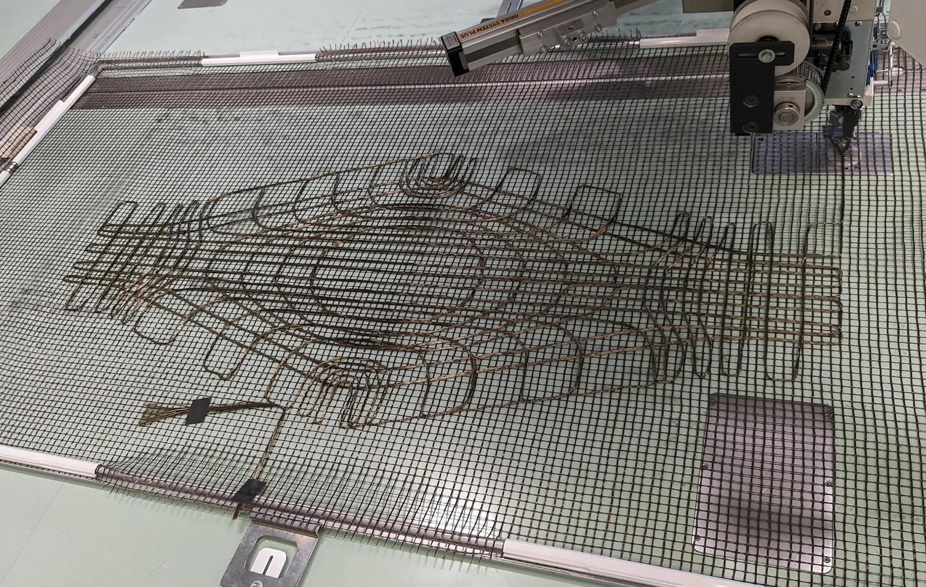 Embroidery machine placing curved basalt fiber courses on a grid carrier